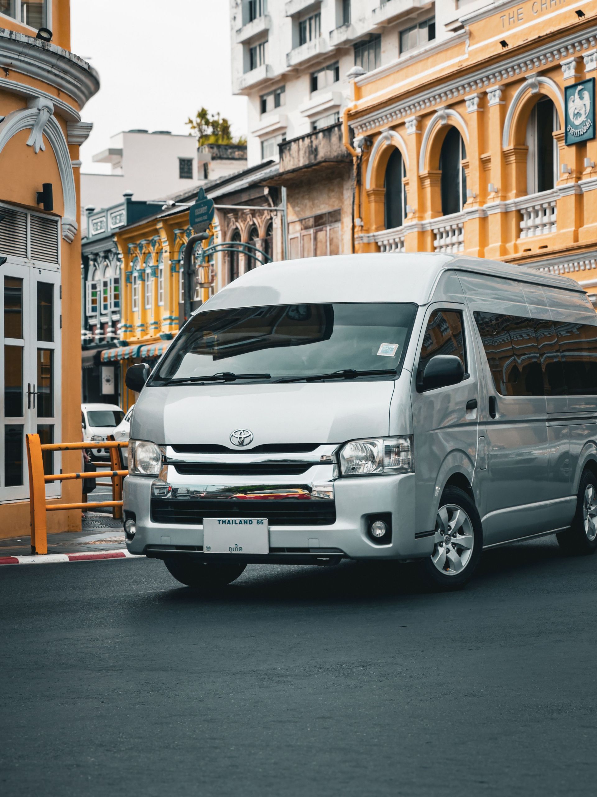 A modern van in front of colorful colonial buildings on a street in Phuket, Thailand.