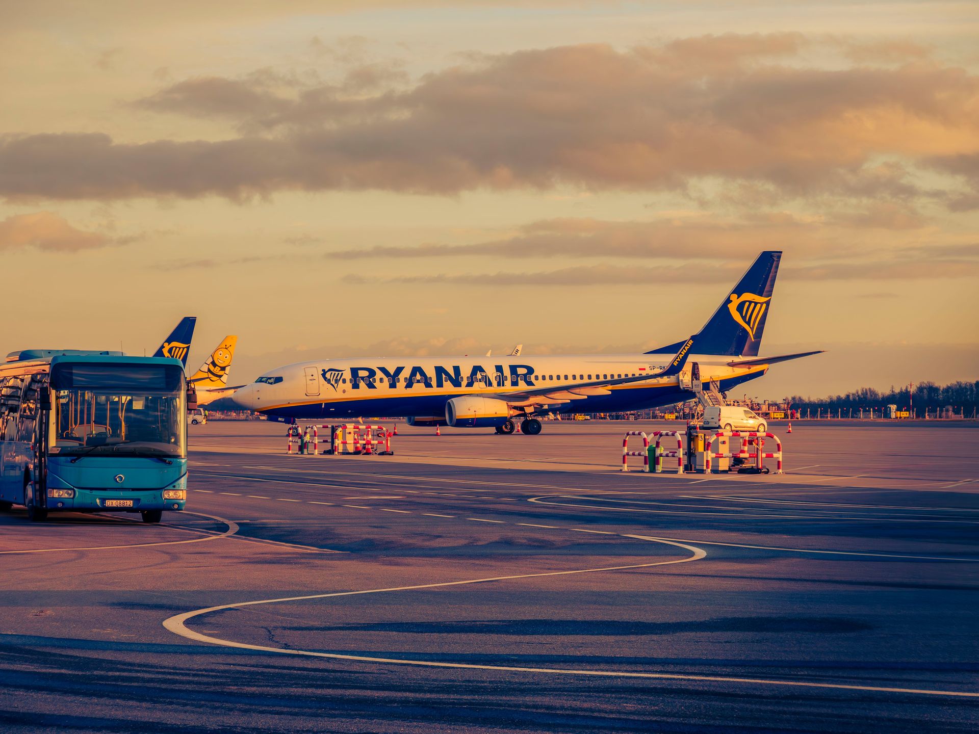 Ryanair aircraft parked at Wrocław airport during sunset, with a shuttle bus in view.