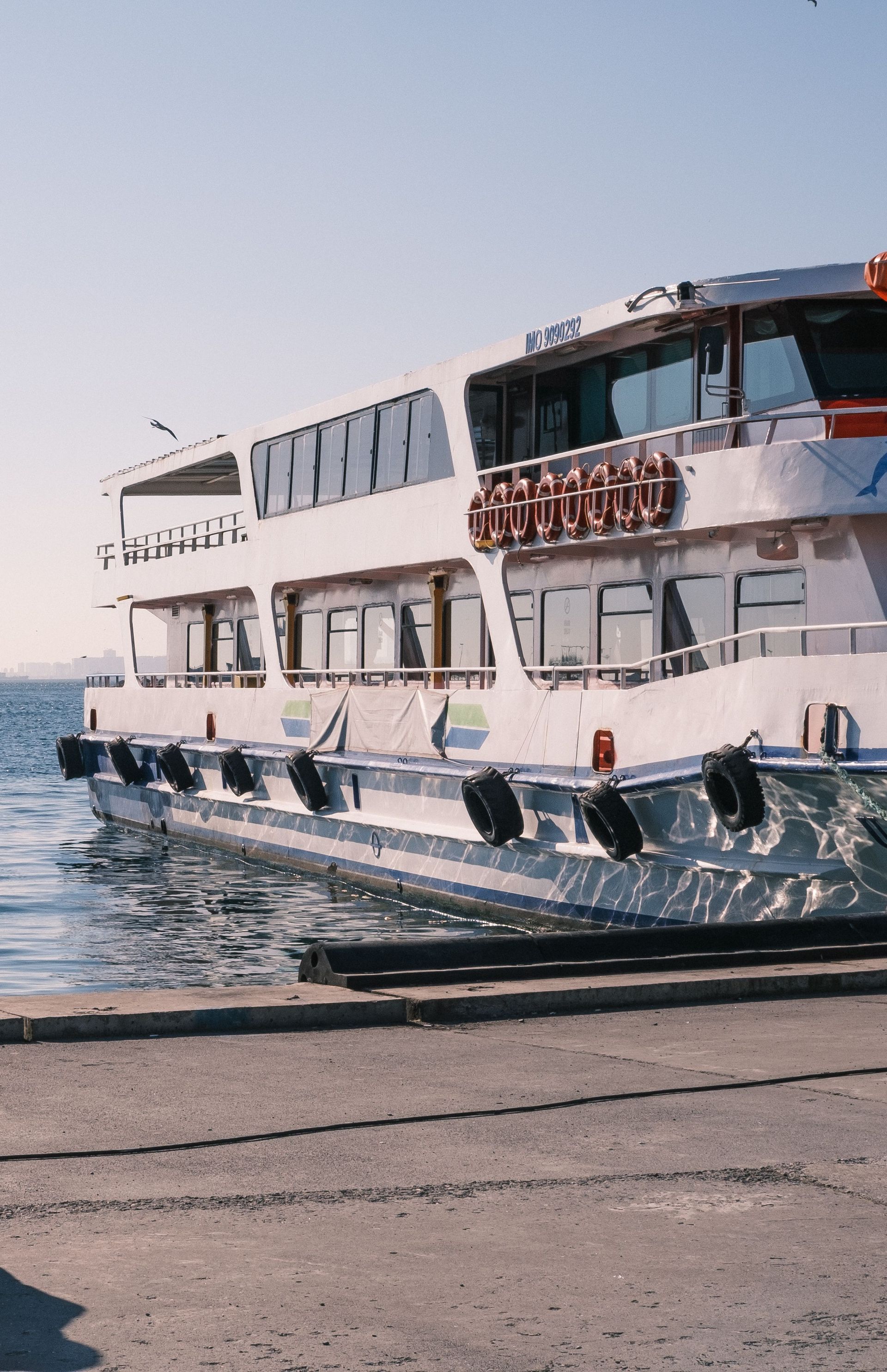 A white passenger ferry is docked at a harbor under clear daylight, ready for boarding.